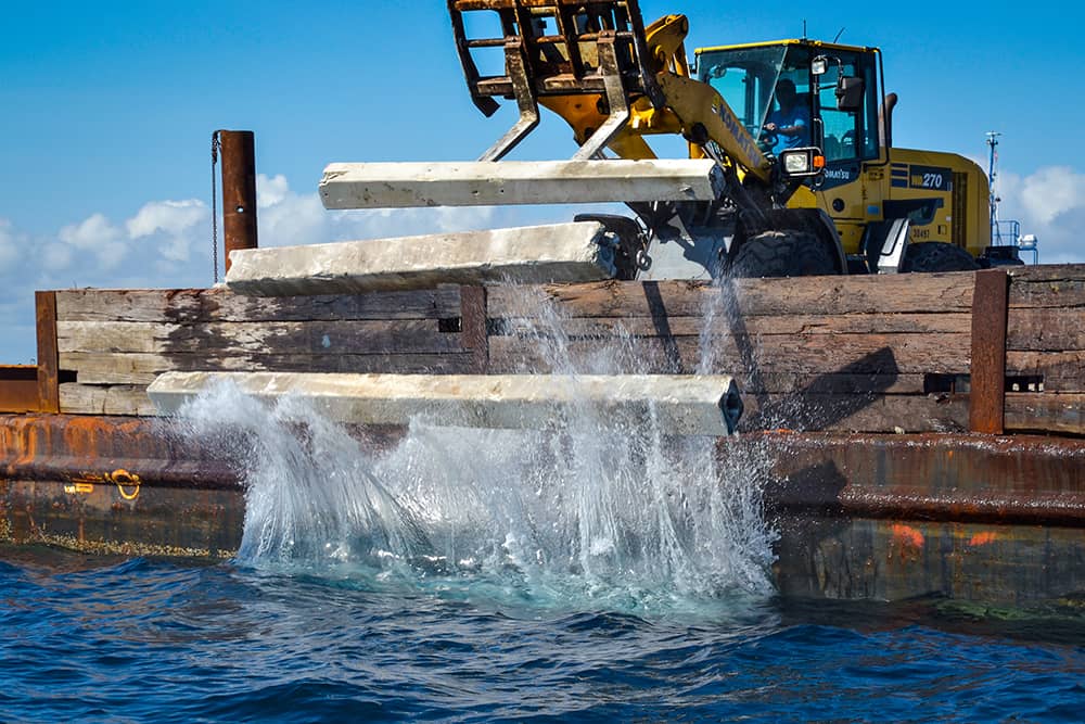 Heavy equipment dropping cement into the ocean to build artificial reef structures