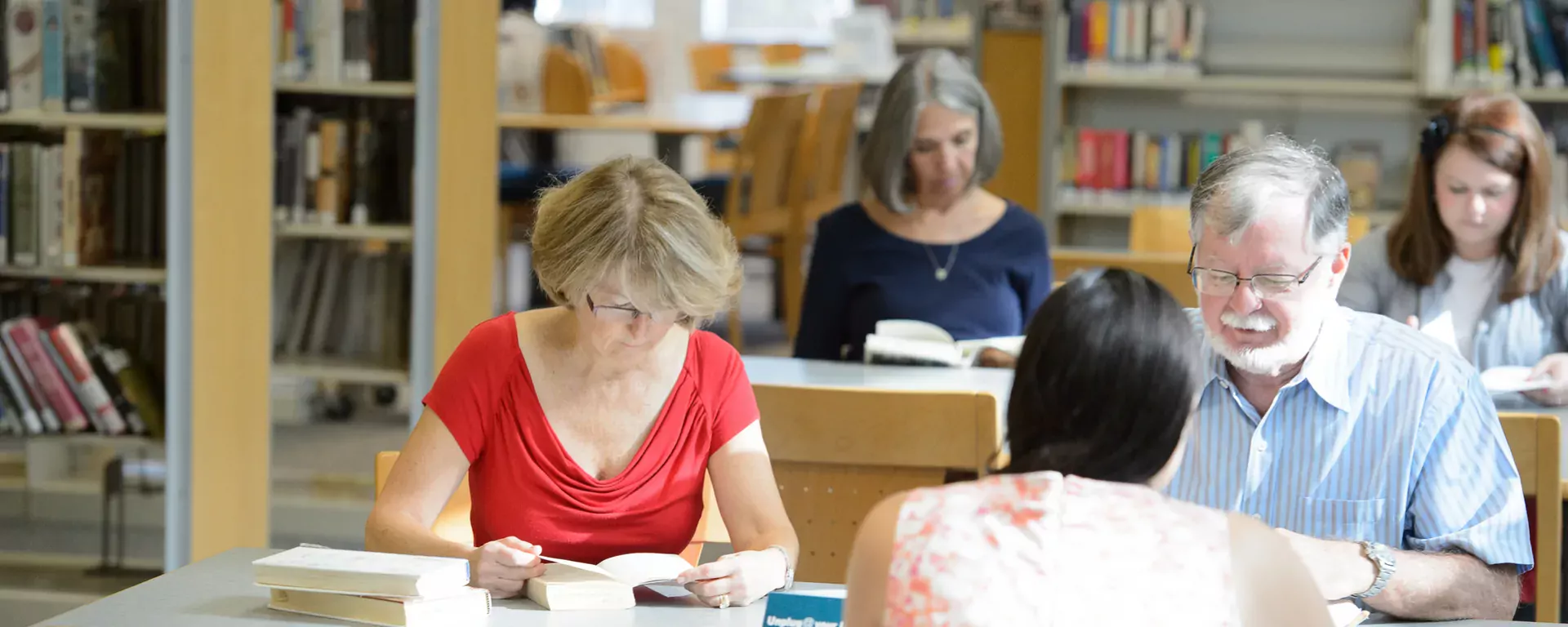 five adults reading while seated at library tables