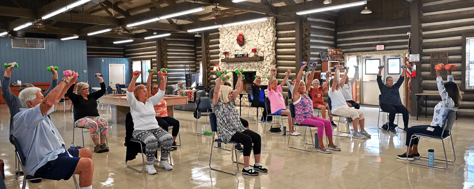 Image of a group of adults participating in a workout with weights chair class at the Log Cabin Senior Center in Jensen Beach, FL.