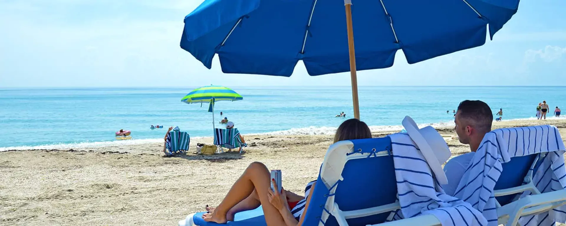 Image of two guests enjoying the rentable beach chairs and umbrellas available at Sand Dune Café in Jensen Beach, FL. 