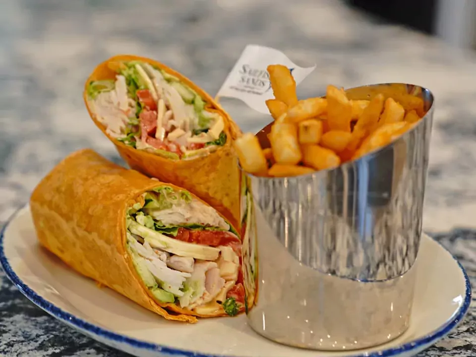 Image of a turkey avocado wrap with a side of fries