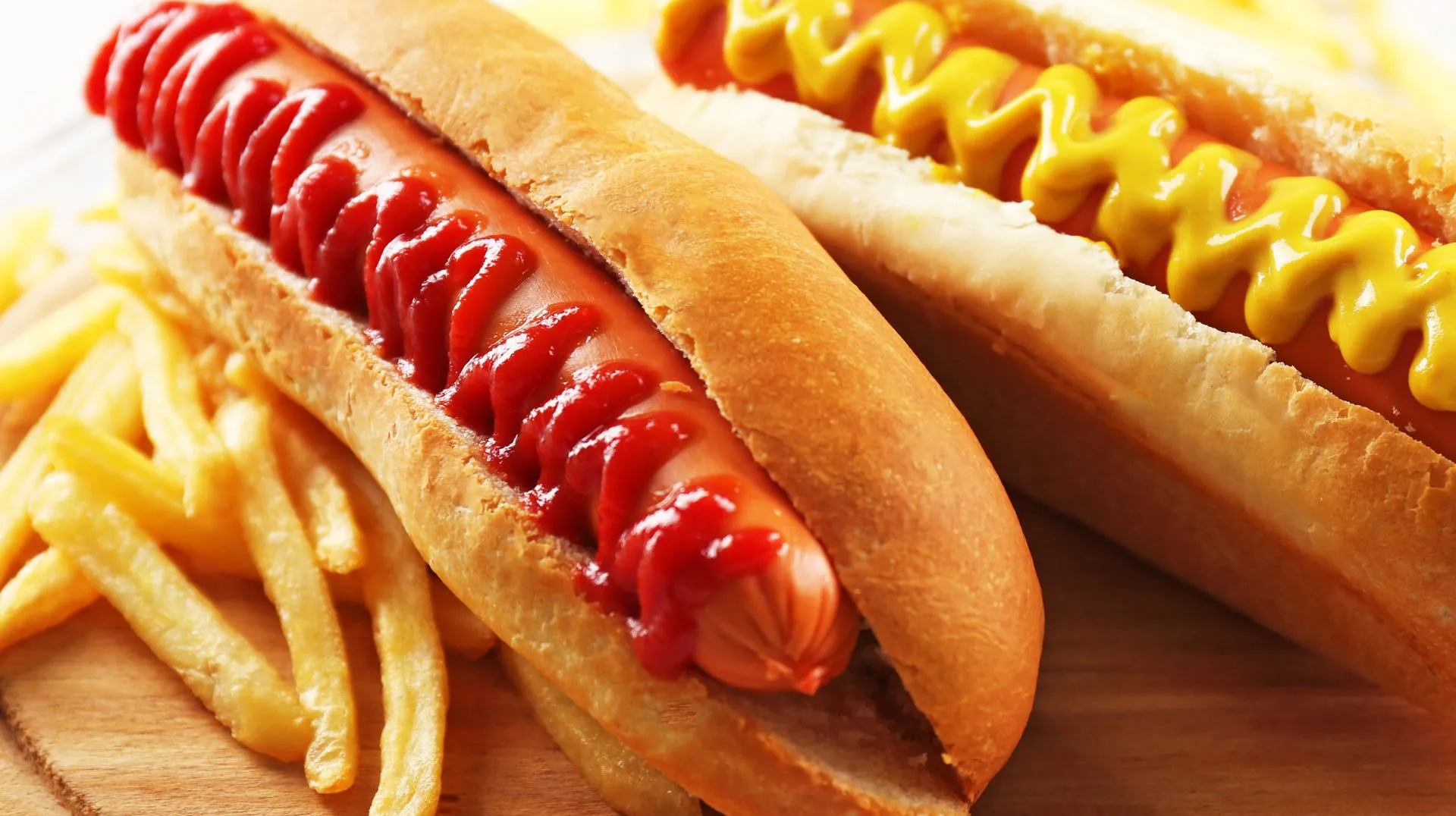 Two hotdogs with ketchup and mustard and a side of fries