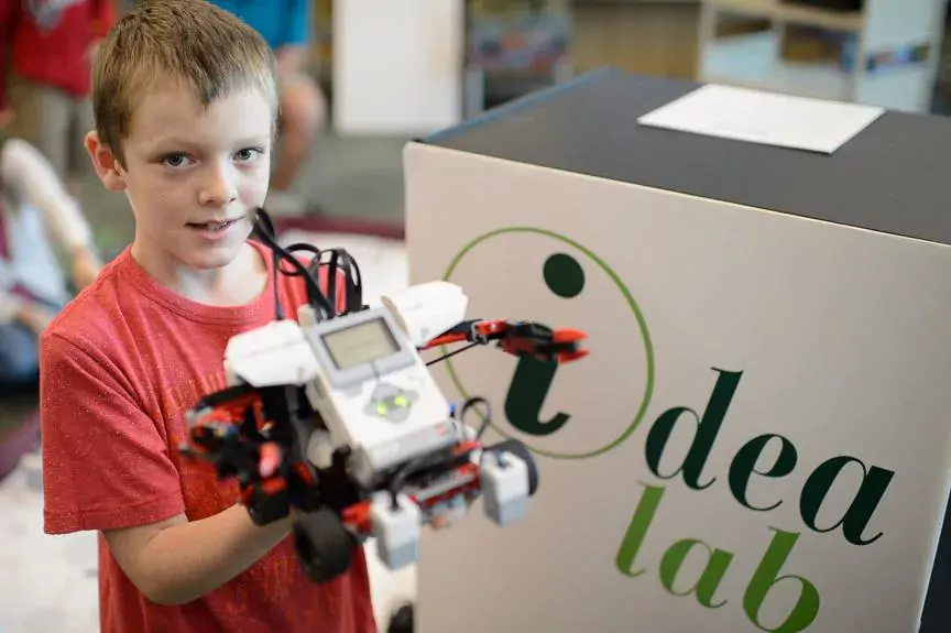 Picture of a young boy proudly displaying a robot he made in an idea lab